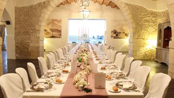 A long dining table set for a formal event, with white chairs and a floral centerpiece.
