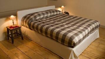 Un lit recouvert d’une couverture à carreaux, une table de chevet avec une lampe et un petit tabouret sur lequel se trouve un objet rouge.
