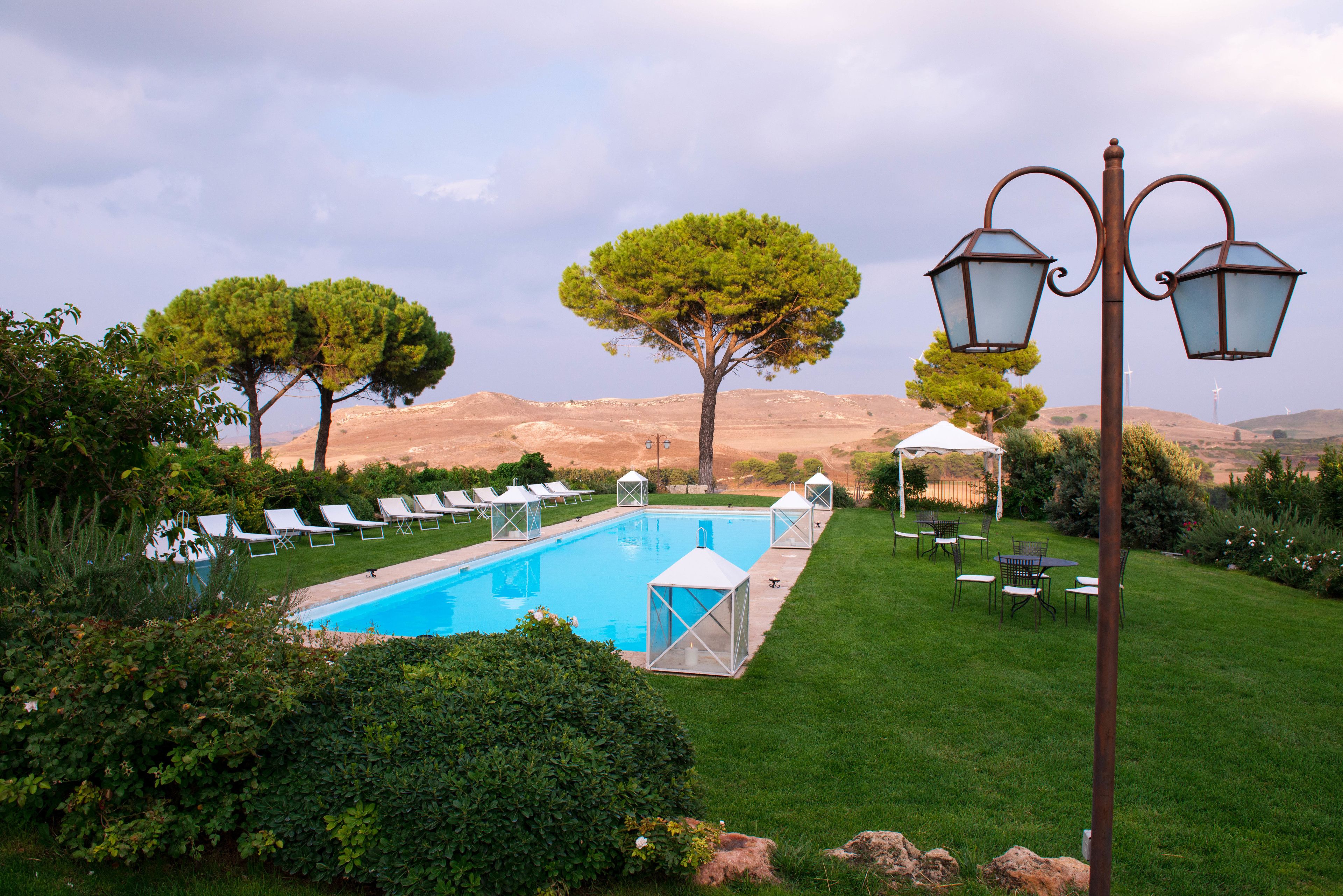 A pool with lounge chairs, a gazebo, and a lamp post in a landscaped garden.