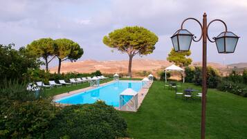 A pool with lounge chairs, a gazebo, and a lamp post in a landscaped garden.