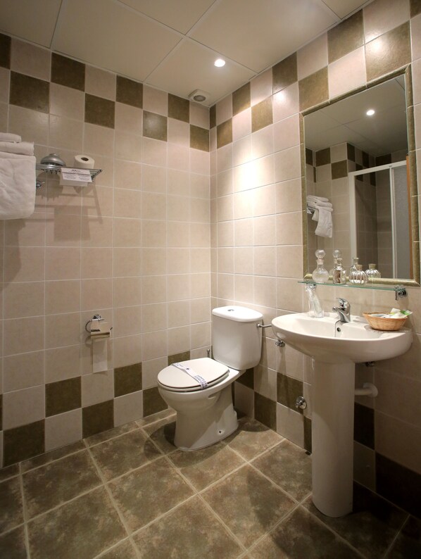 A bathroom with a toilet, sink, and mirror. There are towels hanging on the wall and a basket on the sink. - Hotel Castillo Bonavia (Pedrola)