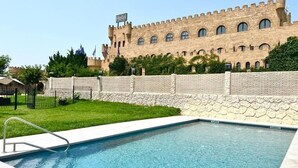 A swimming pool with a castle-like building in the background. - Hotel Castillo Bonavia (Pedrola)