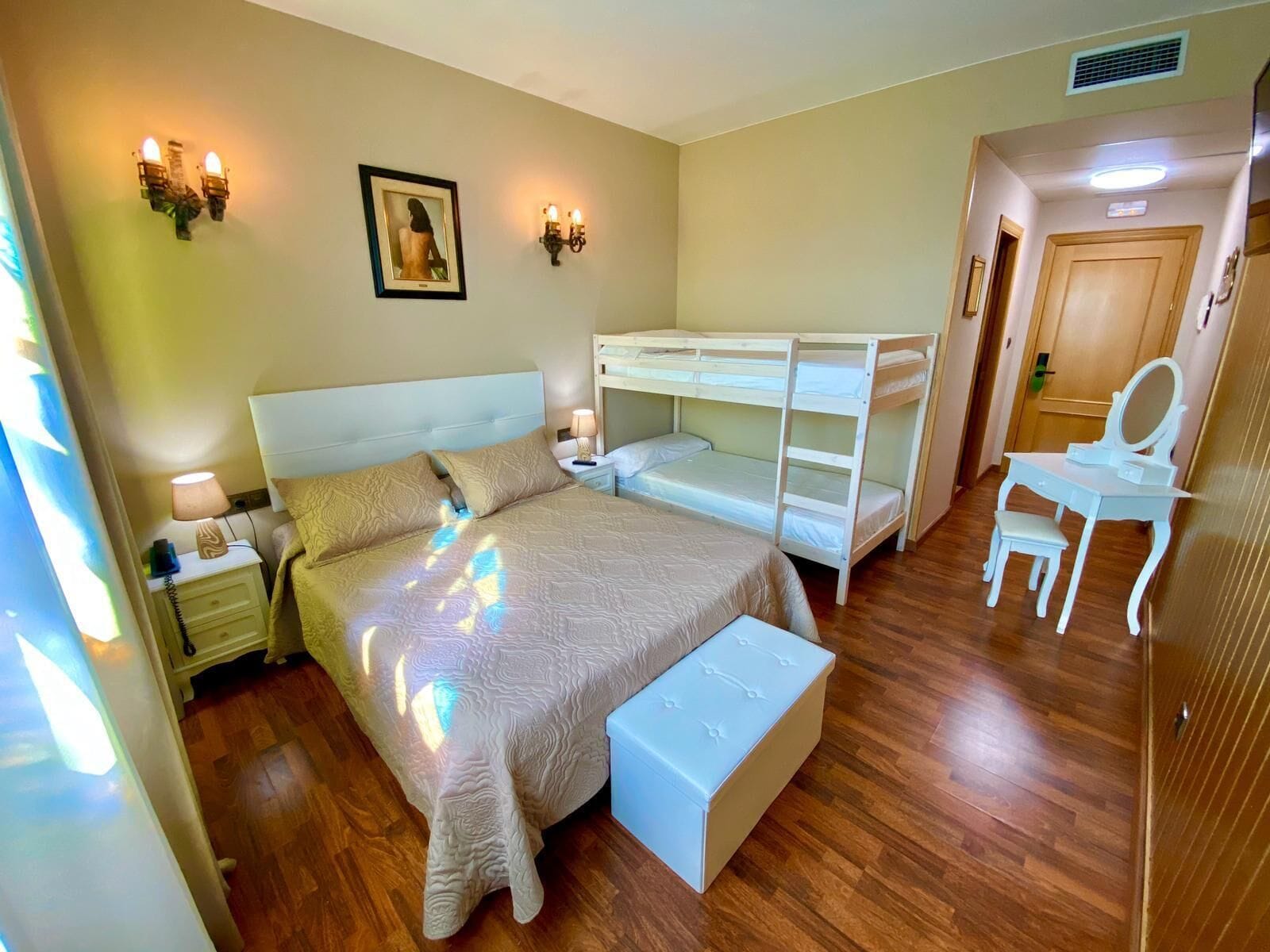 A bedroom with a bunk bed, a desk with a chair, a bedside lamp, and a framed picture on the wall.