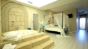 A bedroom with a large bathtub, a bed with a canopy, and a stone wall. - Hotel Castillo Bonavia (Pedrola)