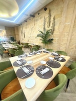 Un restaurante con una larga mesa de madera dispuesta para una comida, rodeada de sillas tapizadas en verde.