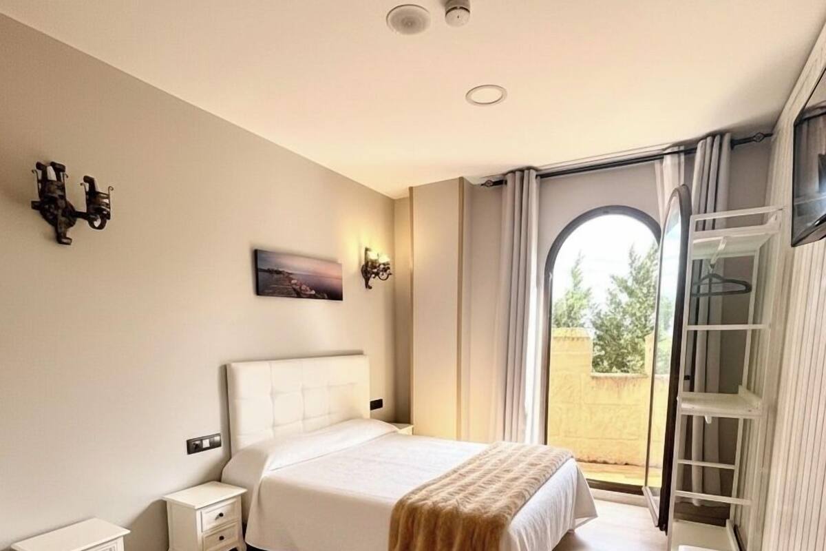 Une chambre à coucher avec un lit, des tables de chevet, une armoire et une vue par la fenêtre.
