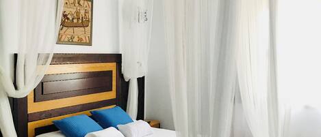 Een bed met een houten hoofdbord, wit beddengoed, blauwe kussens en een hemelbed.