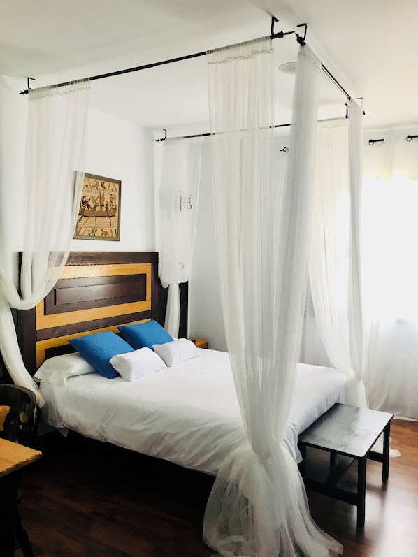 A bed with a wooden headboard, white bedding, blue pillows, and a canopy. - Hotel Castillo Bonavia (Pedrola)