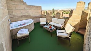 A private outdoor area with a stone wall, a bathtub, wicker furniture, and a table with a bottle and fruit. - Hotel Castillo Bonavia (Pedrola)