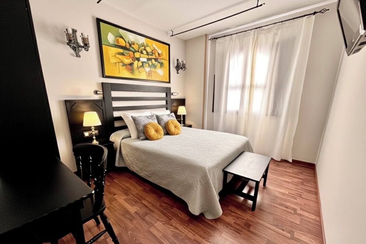 Une chambre à coucher avec un lit, des tables de chevet, un bureau, une chaise et un tableau au mur.