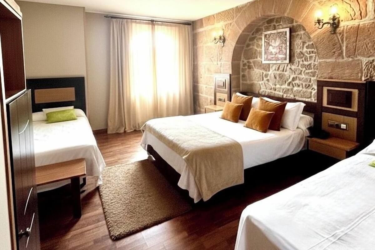 Une chambre d’hôtel avec deux lits, un mur en pierre, une cheminée et une grande fenêtre avec des rideaux.