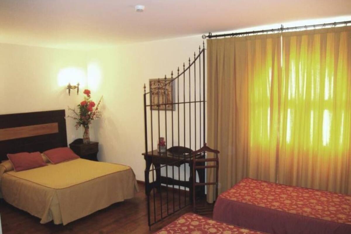 Une chambre d’hôtel avec deux lits, une table de chevet, une petite table avec une chaise, un élément décoratif mural et une fenêtre avec des rideaux.