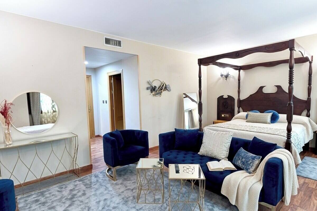 Une chambre à coucher avec un lit à baldaquin, un coin salon avec un canapé et des fauteuils, une petite table et un miroir.