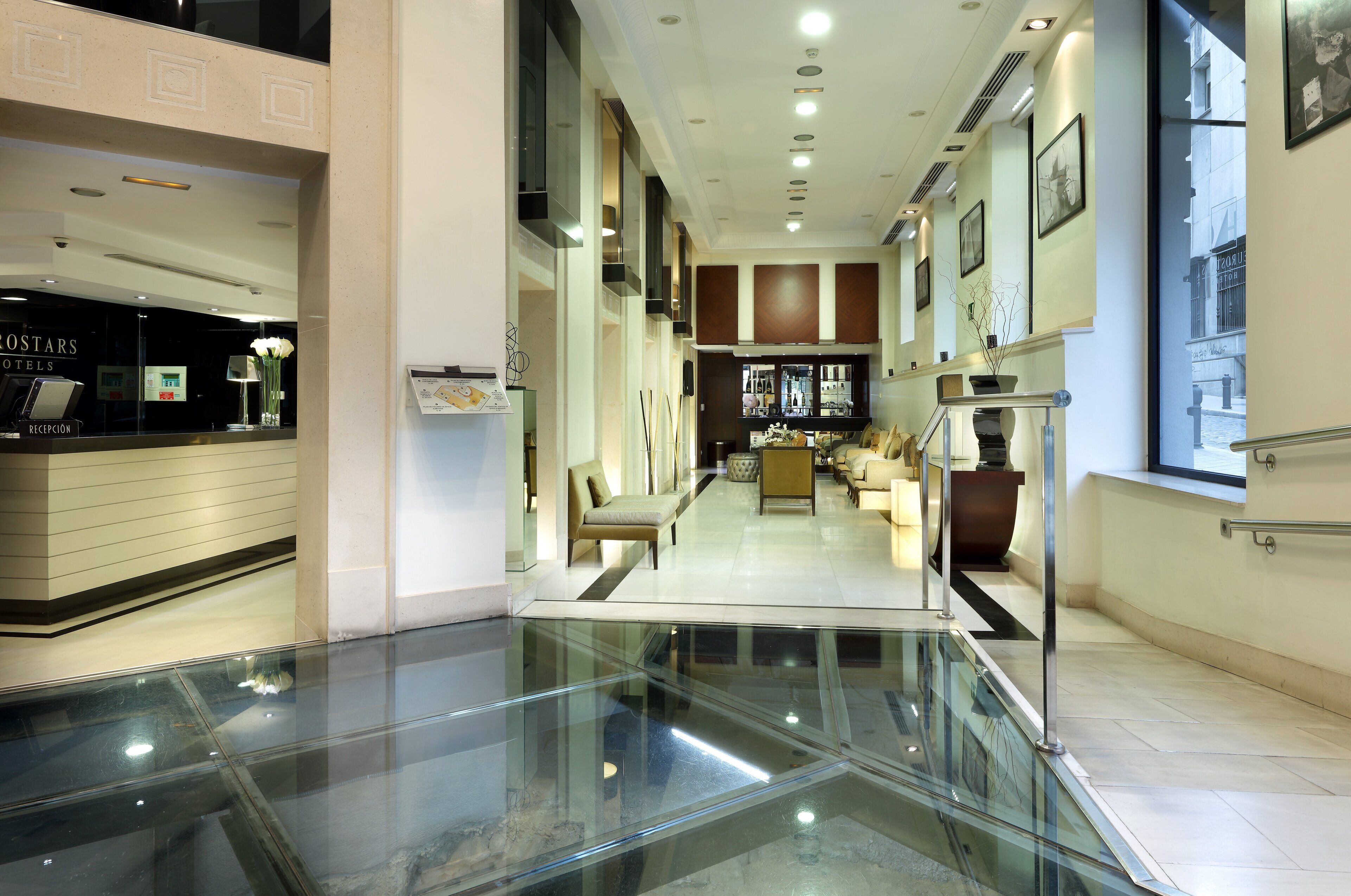 Vestíbulo de hotel con recepción, zona de estar y suelo de vidrio.