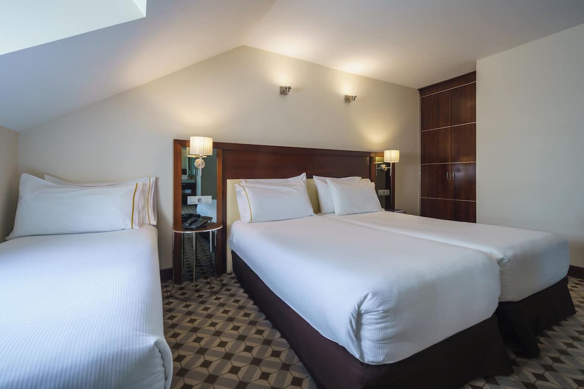 A hotel room with two beds, a small table, and a wardrobe.
