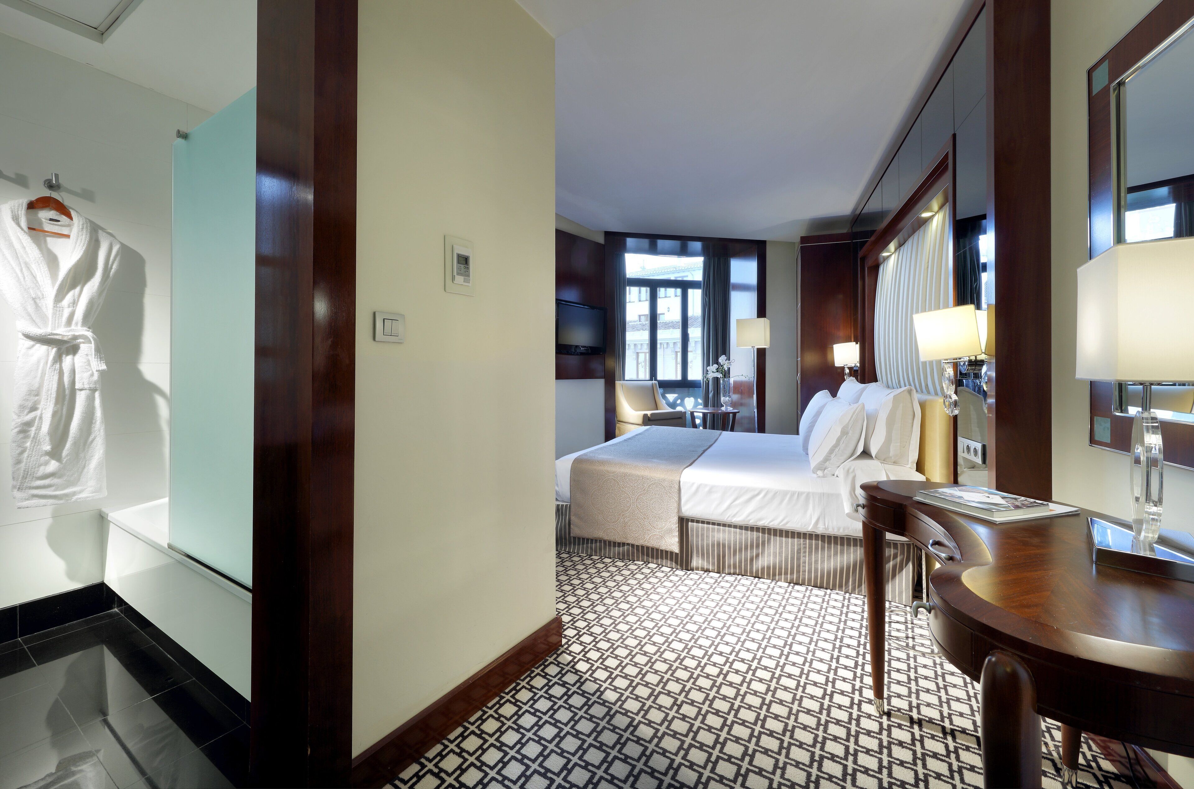 Una habitación de hotel con cama, mesita de noche, lámpara y espejo.