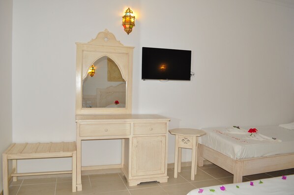 Quarto com cama, mesa de cabeceira, cômoda, espelho e televisão na parede.
