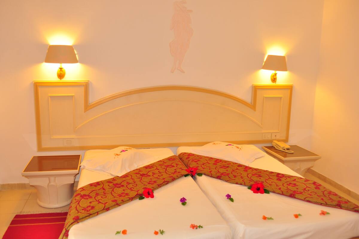 Una habitación de hotel con una cama, dos mesitas de noche y una lámpara en cada una.