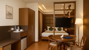 Ein Hotelzimmer mit Bett, Fernseher, Schreibtisch mit Stuhl, einer kleinen Küchenzeile und einem Esstisch.