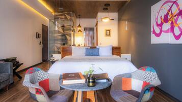 Una habitación de hotel moderna con una cama grande, una ducha de vidrio, una pequeña mesa redonda con sillas y una escalera.