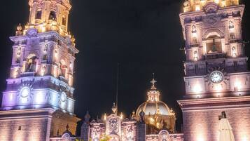 A historic building with illuminated towers and domes, a small tree, and outdoor seating.
