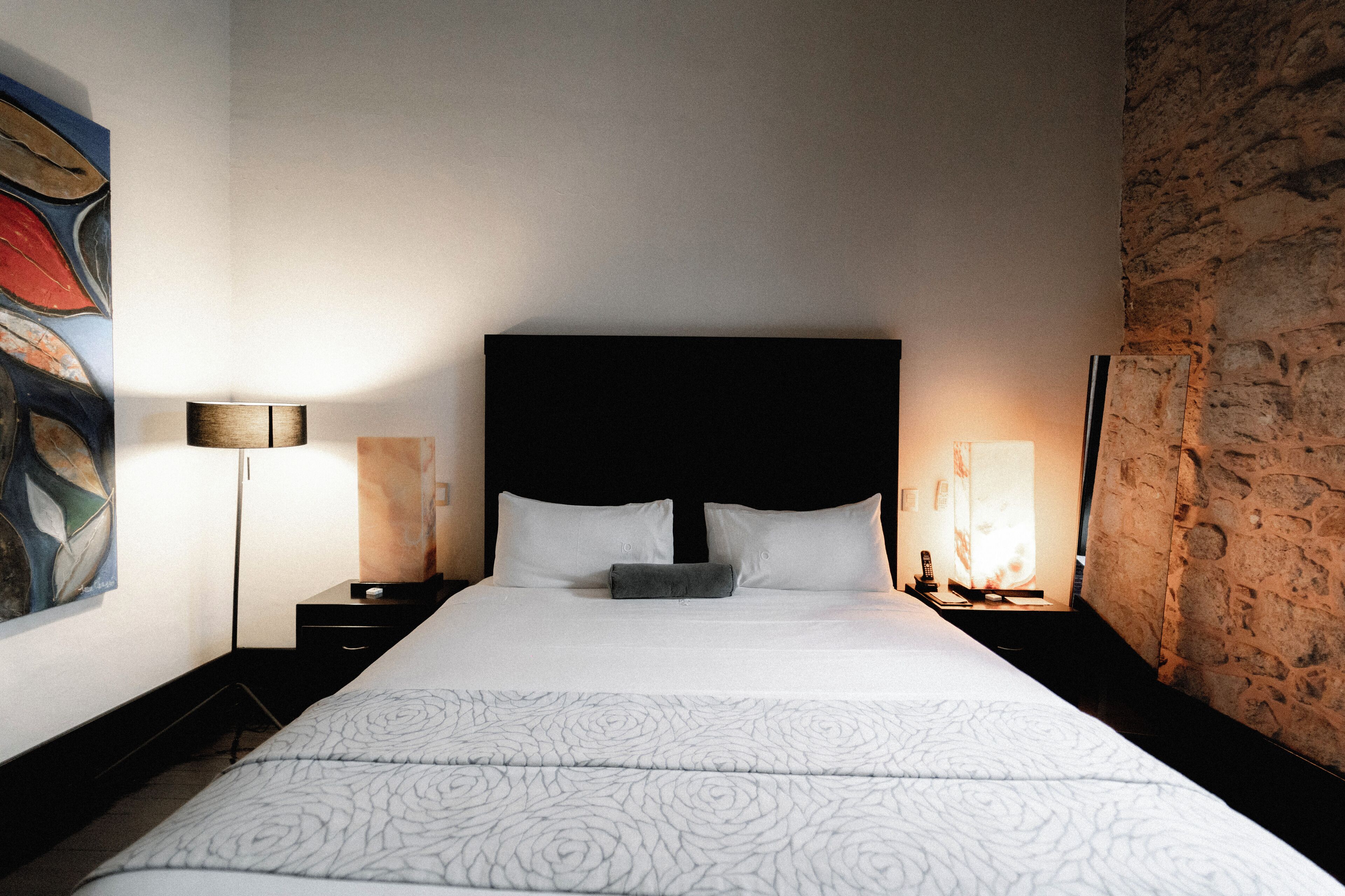 Hotellihuone, jossa on suuri sänky, pääty, kaksi yöpöytää ja seinä, jossa on koristeellinen kivipinta.