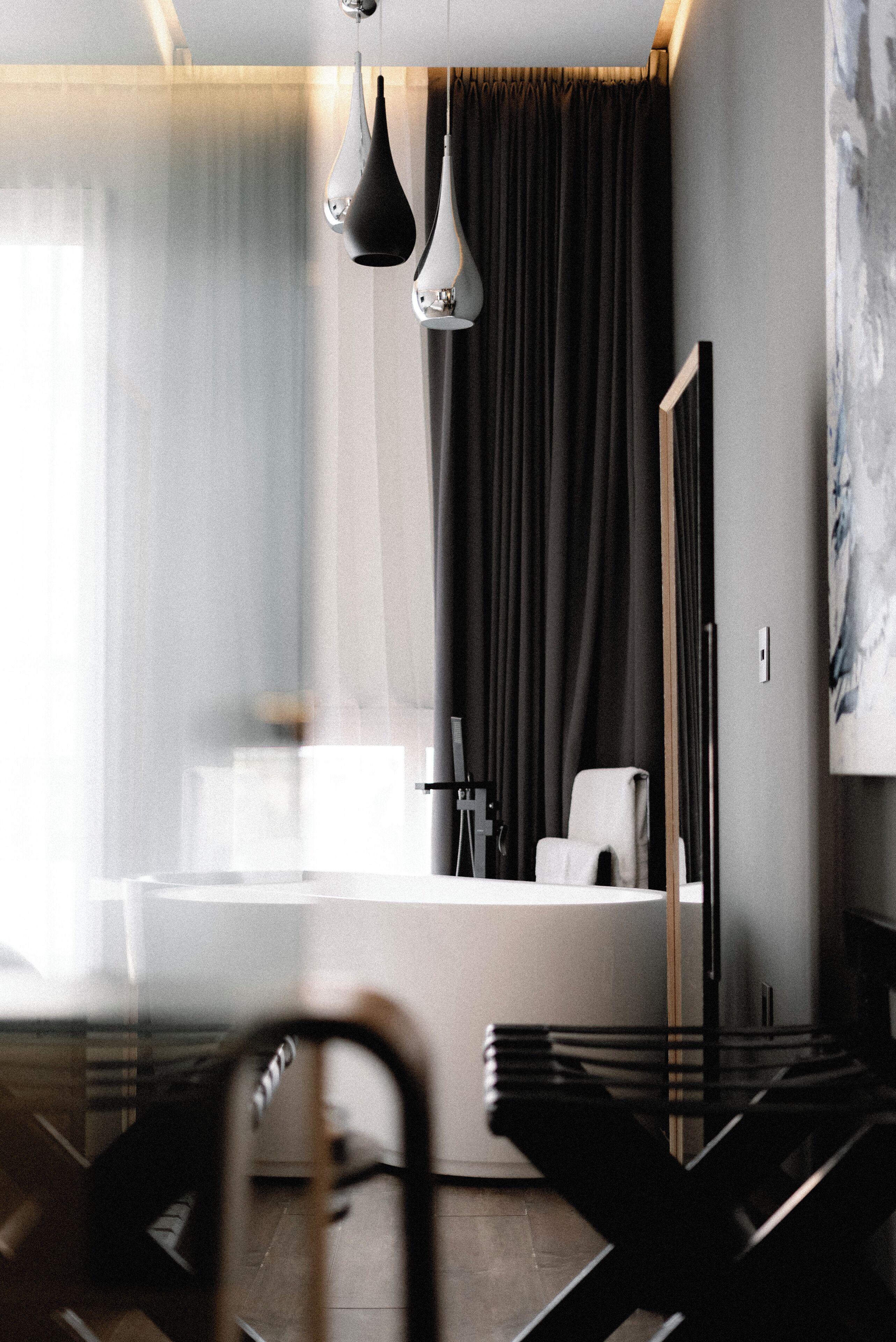 Une chambre d’hôtel moderne avec une grande fenêtre, une chaise noire, un bureau et un miroir.