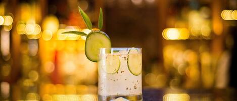 A glass with a drink garnished with cucumber slices and a sprig of rosemary.