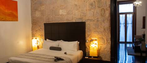 Un dormitorio con pared de piedra, una cama grande con ropa blanca, dos lámparas de noche y un candelabro.