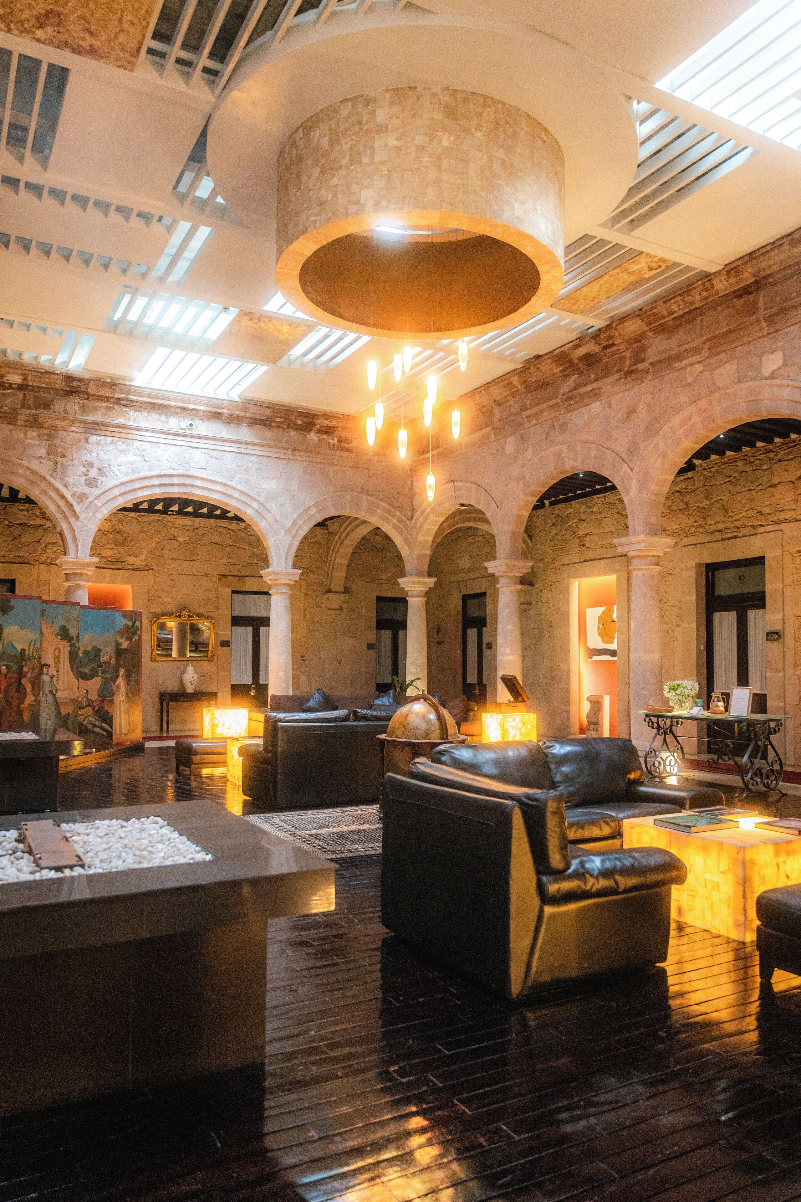 Un hall d’entrée spacieux avec un plafond haut, des arches en pierre et un espace salon central agrémenté de canapés en cuir.