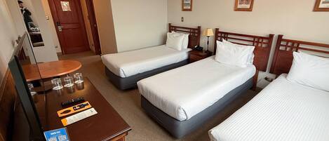 A hotel room with two single beds, a wooden desk with a mirror, a small table with glasses, and a framed picture on the wall.
