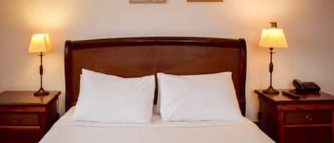A neatly made bed with white linens, two bedside lamps, a wooden headboard, and two framed pictures on the wall.