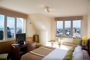A hotel room with a bed, a desk with a television, a window with a city view, and a lamp. - Park Inn by Radisson Puerto Varas (Puerto Varas)