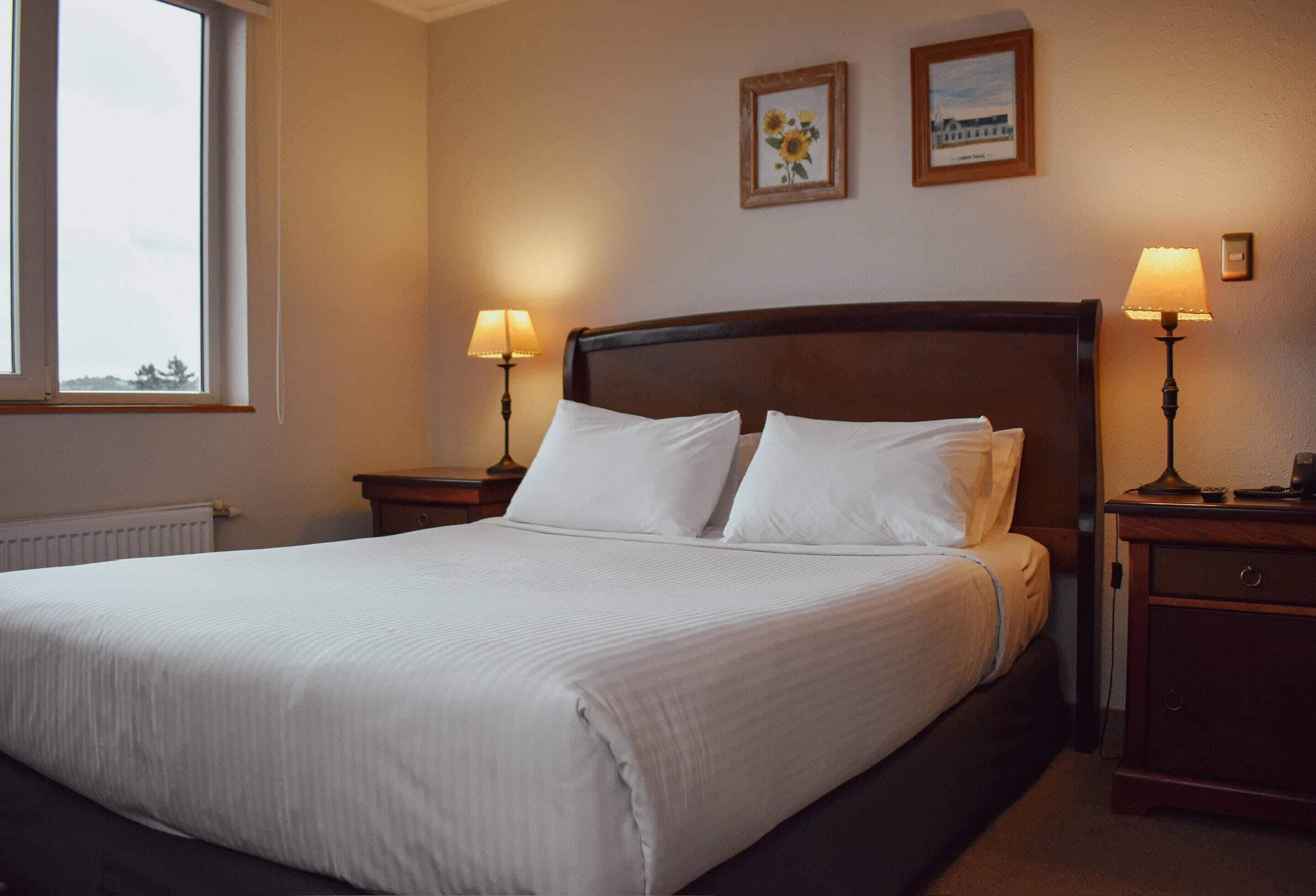 A neatly made bed with white linens, two bedside lamps, and a framed picture on the wall.