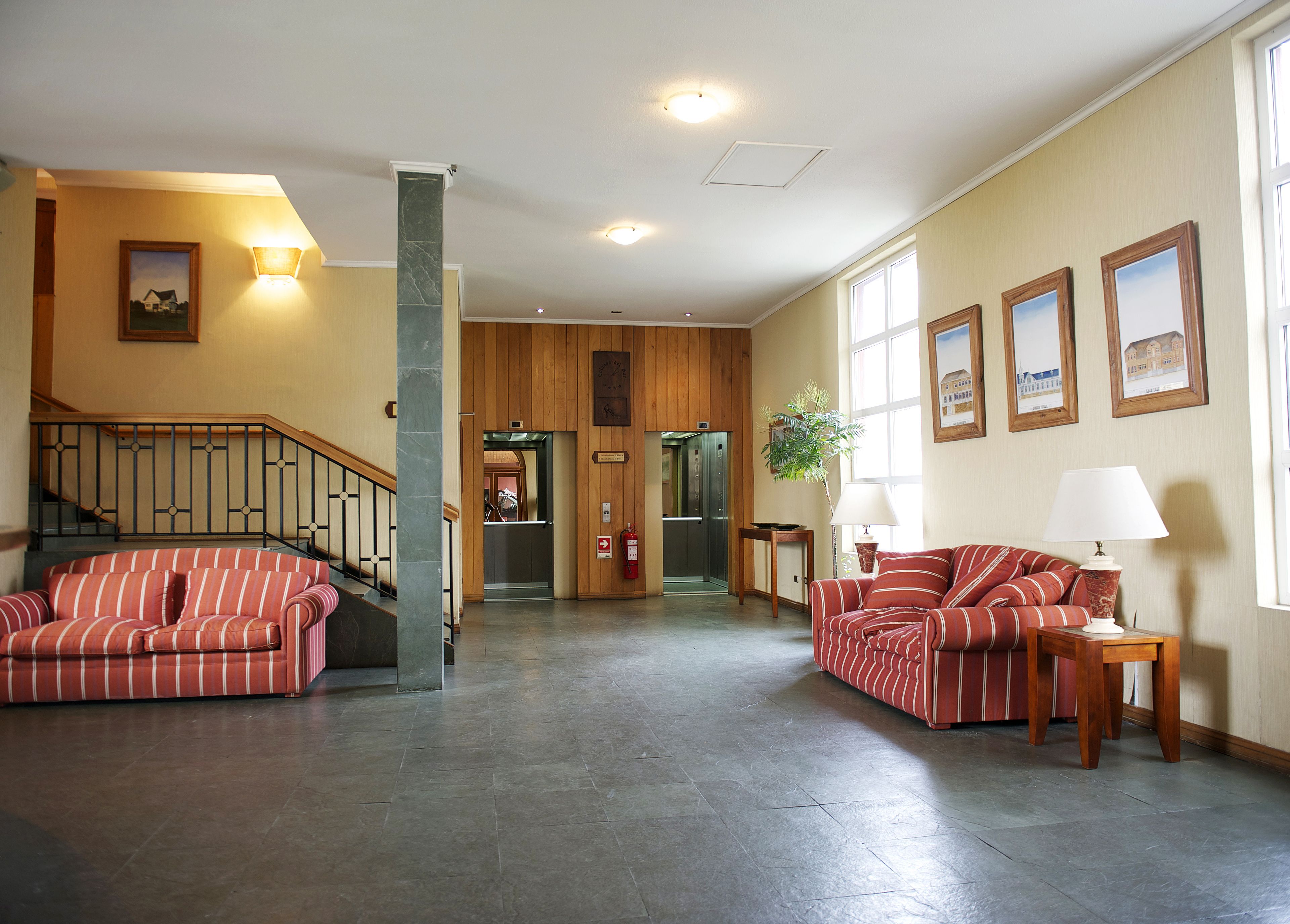 A spacious lobby with a staircase, a reception desk, and a seating area with striped sofas.