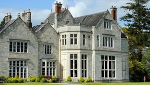 A large stone building with multiple chimneys, large windows, and a well-maintained lawn.