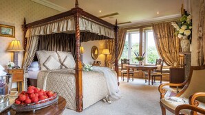 A four-poster bed with a quilted bedspread, a dining table with chairs, and a vase with flowers on a side table.