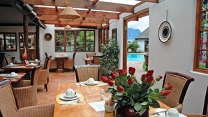 Zona de menjador amb taules i cadires de fusta, un gran vas amb roses vermelles i vista a una piscina i muntanyes.