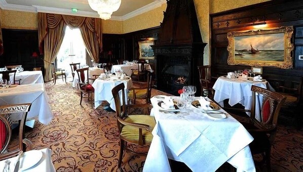 A dining area with tables set for a meal, a fireplace, and a painting on the wall.