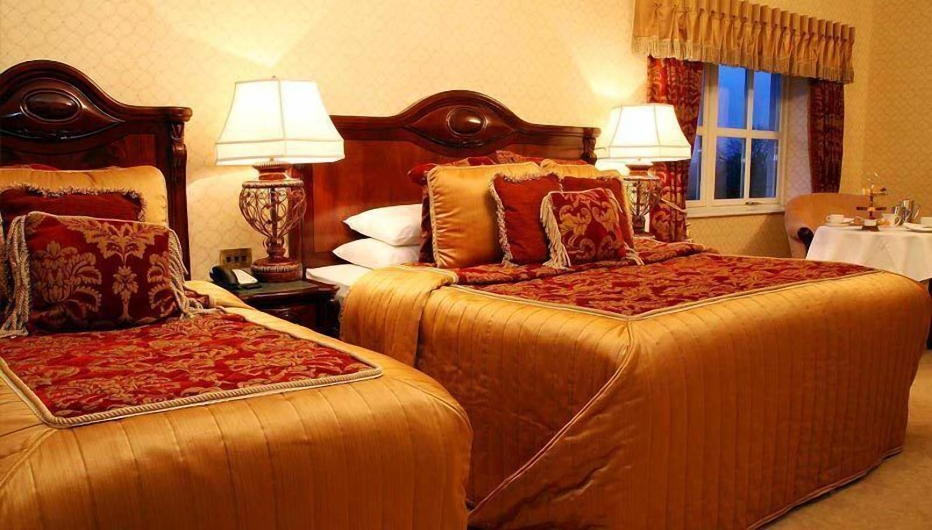 Une chambre d’hôtel avec deux lits, chacun recouvert d’une couvre-lit rouge et or, deux lampes de chevet et une fenêtre avec des rideaux.