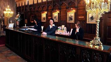 A reception desk with three staff members, framed artwork on the wall, and ornate lighting fixtures.