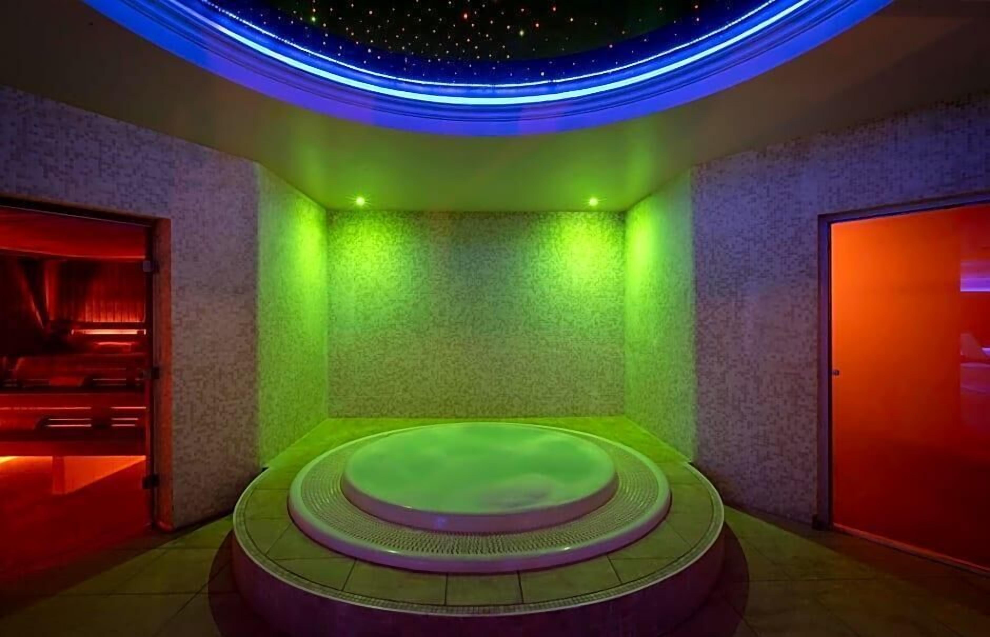 A spa room with a circular hot tub, green ambient lighting, and a starry ceiling design.
