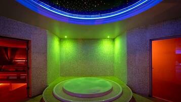 A spa room with a circular hot tub, green ambient lighting, and a starry ceiling design.