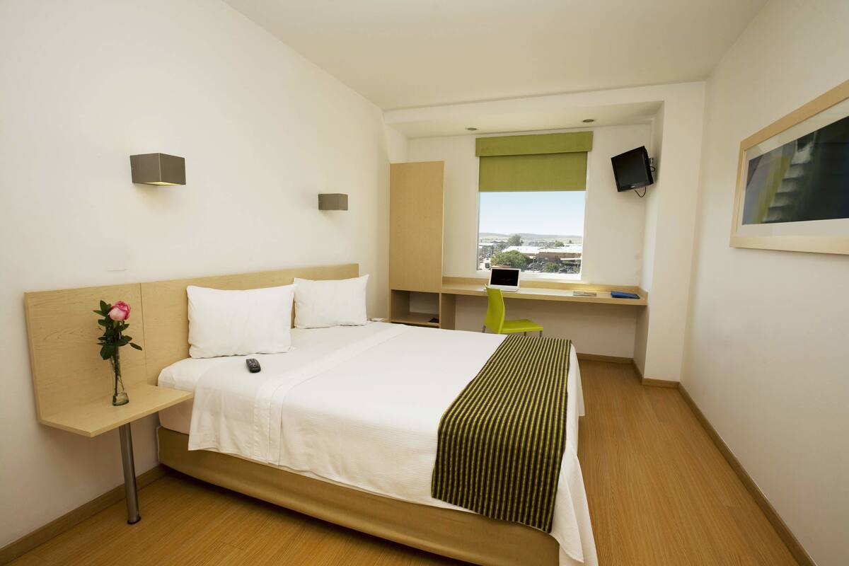 Una habitació d'hotel amb un llit, una taula de nit, un escriptori amb una cadira, una televisió i una finestra que ofereix vistes.