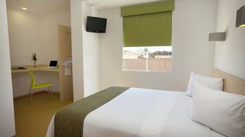 A hotel room with a bed, a desk, a chair, a TV, and a window with a view.
