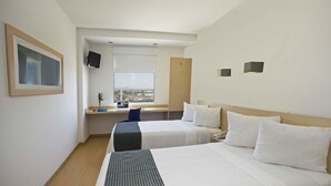 A hotel room with two beds, a desk, a chair, a TV, and a window with a city view. - One Aguascalientes Sur (Aguascalientes)