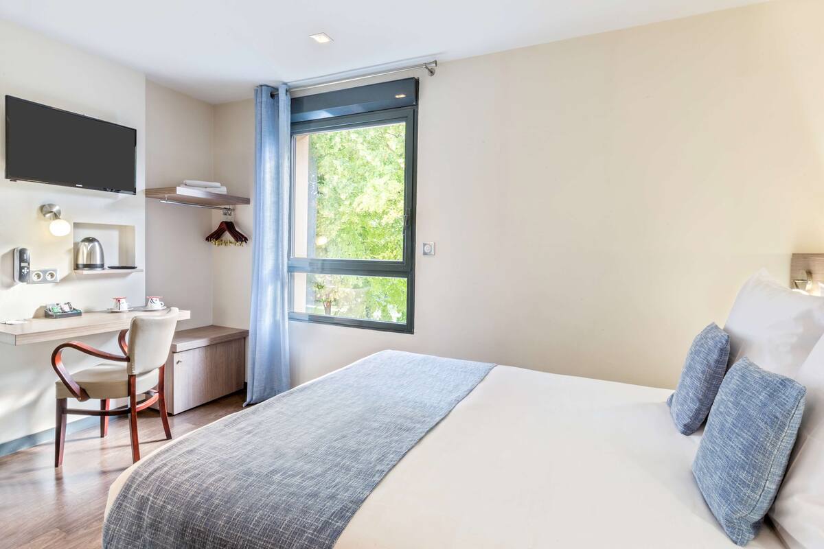 Habitación de hotel moderna con una cama grande, un escritorio con silla, un televisor de pantalla plana y un ventanal con vista a zonas verdes.