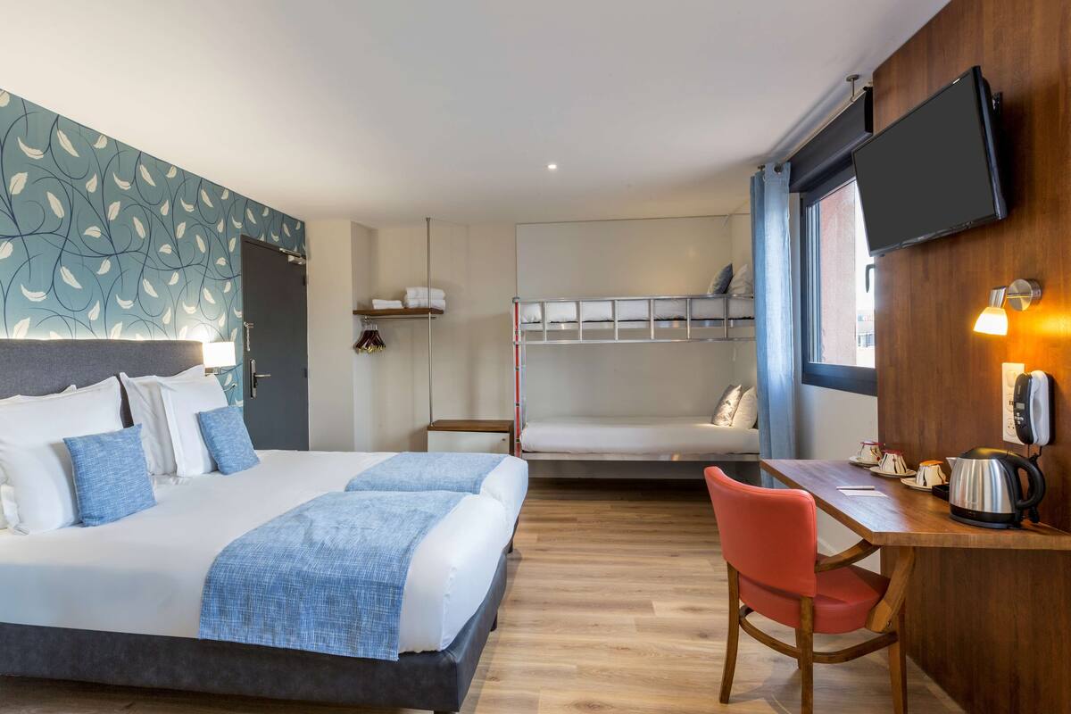 Una habitación de hotel moderna con una cama grande, un escritorio con una silla, una litera y un televisor de pantalla plana montado en la pared.