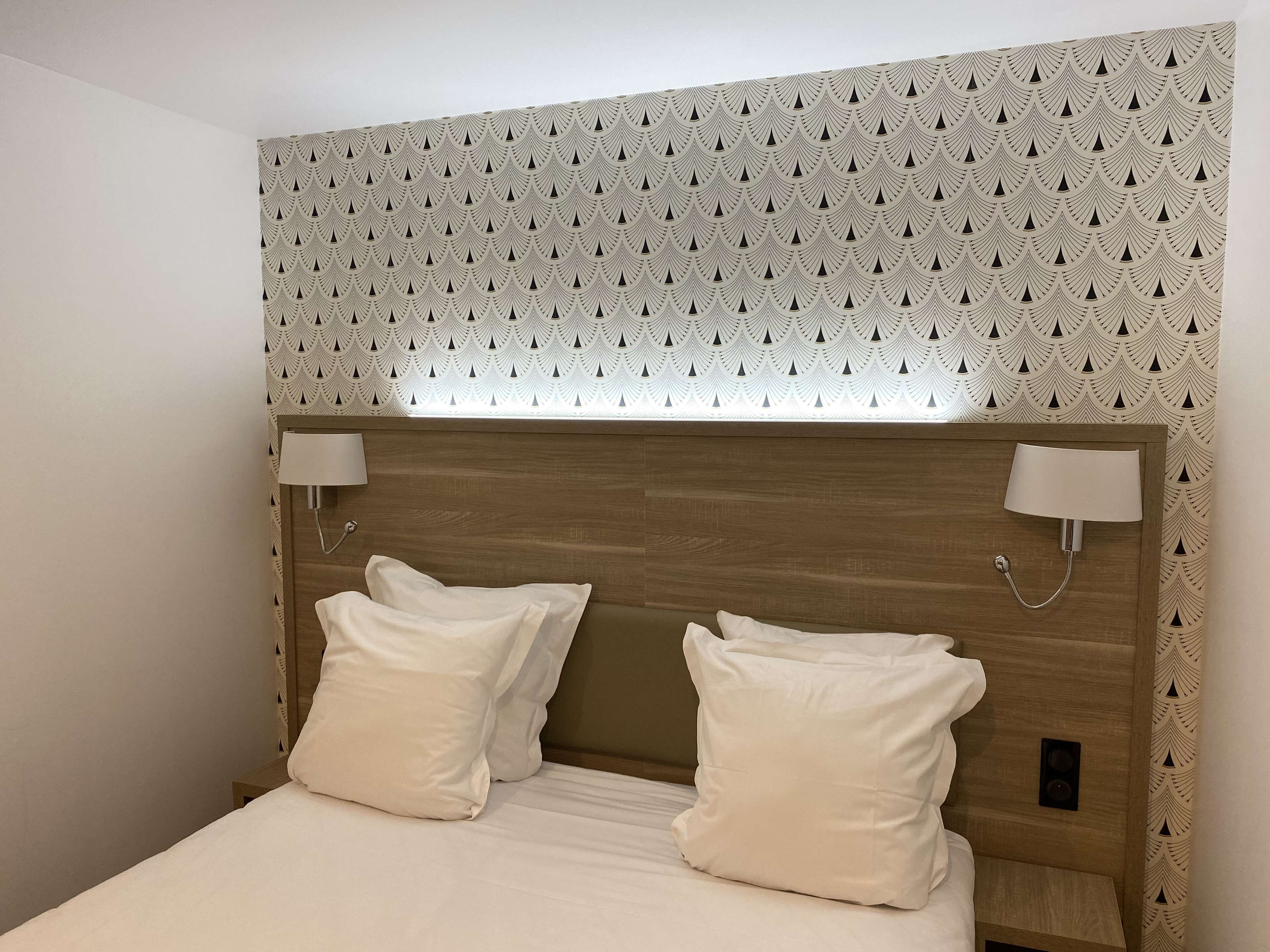 Un letto rifatto con due cuscini e una testiera in legno, con una carta da parati decorata sopra.