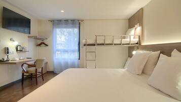 A bedroom with a bunk bed, a desk with a chair, a TV mounted on the wall, and a window with curtains.
